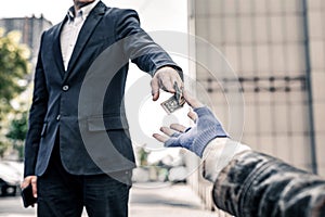 Generous good-looking man in dark costume sharing his money with homeless