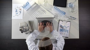 Genetics scientist conducting medical studies of DNA, typing on laptop, top view photo