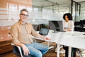 A genial senior business leader sits at an office table with a laptop photo