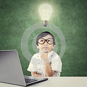 Genius child with laptop thinks idea under lamp