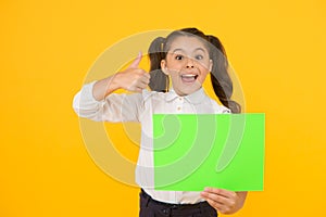 This is genius. Happy girl genius holding blank paper sheet on yellow background. Genius child giving thumbs up gesture