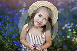 Gentle beautiful girl with an angel look in a hat. A child in a meadow of bright blue wild cornflower.