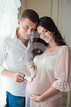 Gentle beautiful pregnant couple near tulle curtains