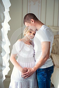 Gentle beautiful pregnant couple near tulle curtains