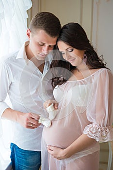 Gentle beautiful pregnant couple near tulle curtains