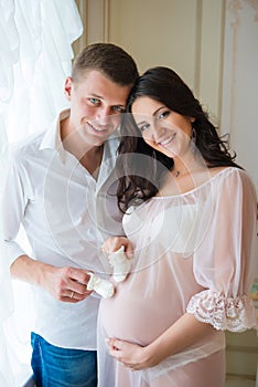 Gentle beautiful pregnant couple near tulle curtains