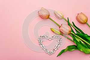 Gentle bouquet of tulips and wooden openwork heart isolated on light pink background