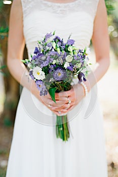 Gentle bride holding a wedding bouquet with blue and white asters, lisiantuses and lavender in her hands, close-up