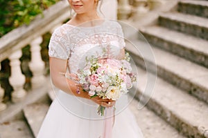 Gentle bride with a wedding bouquet in her hands standing on the ancient stairs of the temple in Prcanj