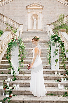 Gentle bride with a wedding bouquet near the columns decorated with flowers and candles on the ancient stairs of the