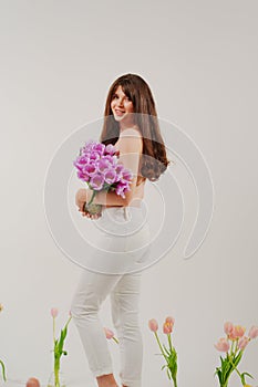 a gentle brunette topless in a room with bouquets of tulips on floor. rear view