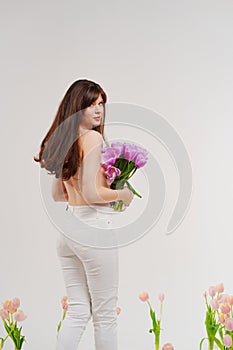 a gentle brunette topless in a room with bouquets of tulips on floor. rear view