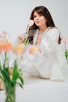 gentle brunette in white sits on the floor with vases of tulips