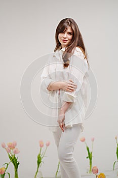 gentle brunette in white stands in a room with bouquets of tulips on the floor
