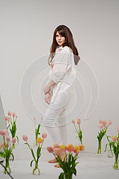 gentle brunette in white stands in a room with bouquets of tulips on the floor