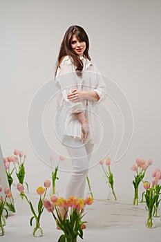 gentle brunette in white stands in a room with bouquets of tulips on the floor