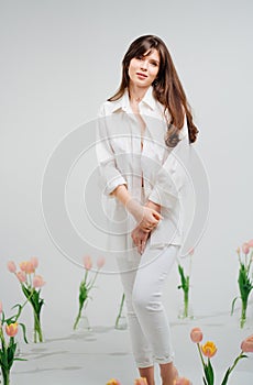 gentle brunette in white stands in a room with bouquets of tulips on the floor