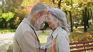 Gentle cuddling of happy smiling married couple senior husband mature wife touching foreheads romance love in park old