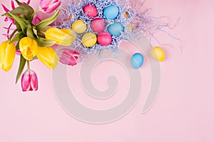 Gentle elegant soft pastel easter decoration - painted eggs, yellow tulips, cupcake on pink background, copy space, top view.