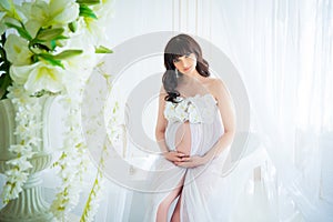 Gentle expectation of motherhood. Beautiful pregnant in light white dress with orchids