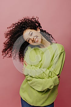 Gentle fair-skinned young girl leaning on her shoulder, smiles flirty toothy on pink background.