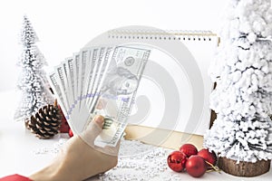 Gentle hands cradle money with a white screen mock-up and White calendar with a festive scene of a beautiful Christmas tree