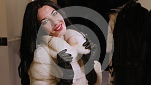 A gentle happy girl tries on a new fur coat made of white fur in the store.