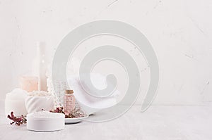 Gentle pink cosmetics oil, small flowers and white soap, cream, clay, towel on white wooden shelf, copy space, vertical.