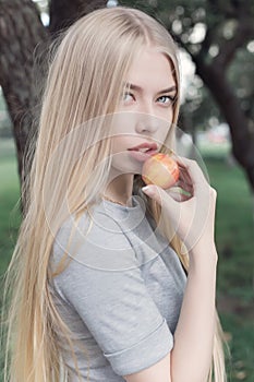 Gentle portrait of a beautiful cute girl with long blond hair with full lips and blue eyes with apple in hand, look at the camera