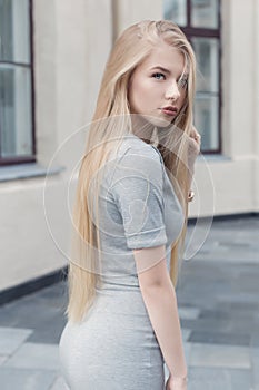 Gentle portrait of a beautiful cute girl with long blond hair with full lips and blue eyes in a gray suit, look at the camera