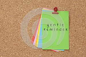 Gentle Reminder written on color sticker notes over cork board b