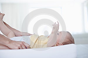 The gentle touch of a mother. A cute baby boy looking up at his mother as she changes his diaper.