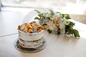 A gentle voluminous bouquet of the bride in white-orange tones and a wedding cake with white cream, adorned with orange fruits