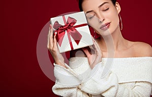 A gentle young lady holds a gift of a face face on a red background