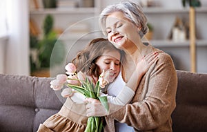 Gently little girl giving flowers and gift to grandmother