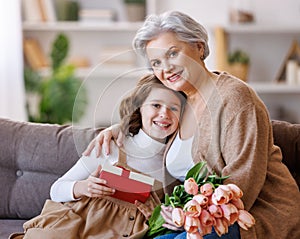 Gently little girl giving flowers and gift to grandmother