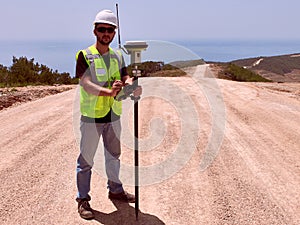 Geodetic engineer surveyor in white hard hat doing measurements with GNSS satellite receiver photo