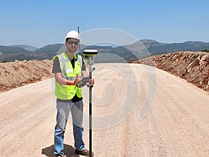 Geodetic engineer surveyor in white hard hat doing measurements with GNSS satellite receiver photo