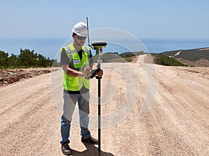 Geodetic engineer surveyor in white hard hat doing measurements with GNSS satellite receiver photo