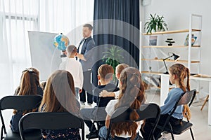 Geography lesson. With globe in hands. Group of children students in class at school with teacher