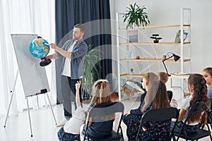 Geography lesson. With globe in hands. Group of children students in class at school with teacher