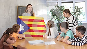 Geography lesson in school class - teacher talks about Catalonia, holding a flag in his hands