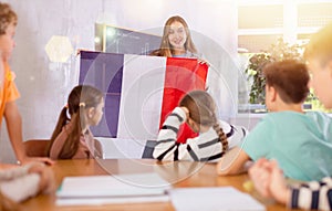 Geography lesson in school class - teacher talks about France, holding flag in his hands