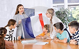 Geography lesson in school class - teacher talks about France, holding flag in his hands
