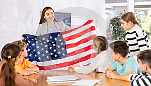 Geography lesson in school class - teacher talks about United States of America, holding flag in his hands