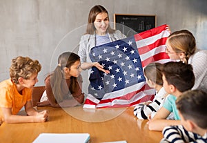 Geography lesson in school class - teacher talks about United States of America, holding flag in his hands