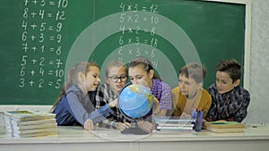 Geography lesson. Schoolmates are studying the globe on the background of a school board