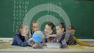 Geography lesson. Schoolmates are studying the globe on the background of a school board