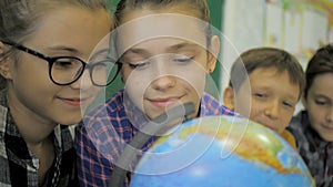 Geography lesson. Schoolmates are studying the globe on the background of a school board