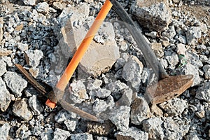 Geological pick with orange handle on the stones next to old hammer